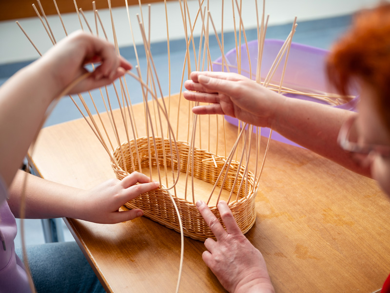 Kind und Erwachserer flechten einen kleinen Korb