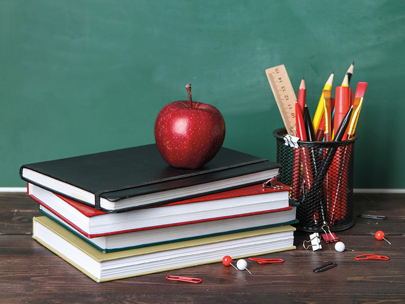 Schulmaterialien mit einem Apfel vor einer Schultafel